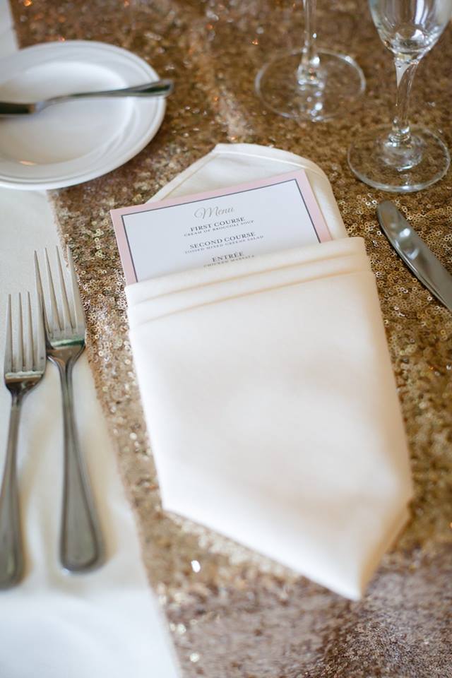 A placesetting at a wedding showing designed menu cards wrapped in a napkin